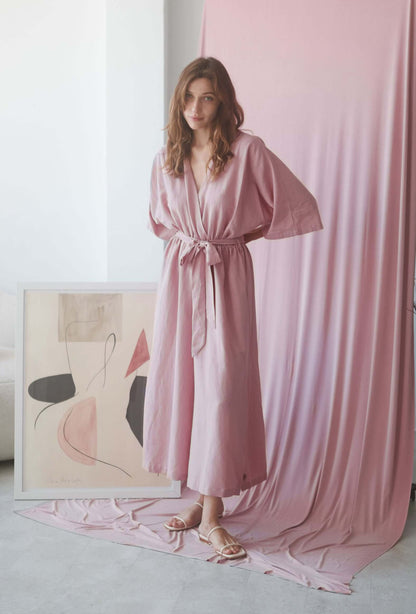 Model wearing a rose kimono jumpsuit with a belt, featuring a soft pink backdrop and abstract art.